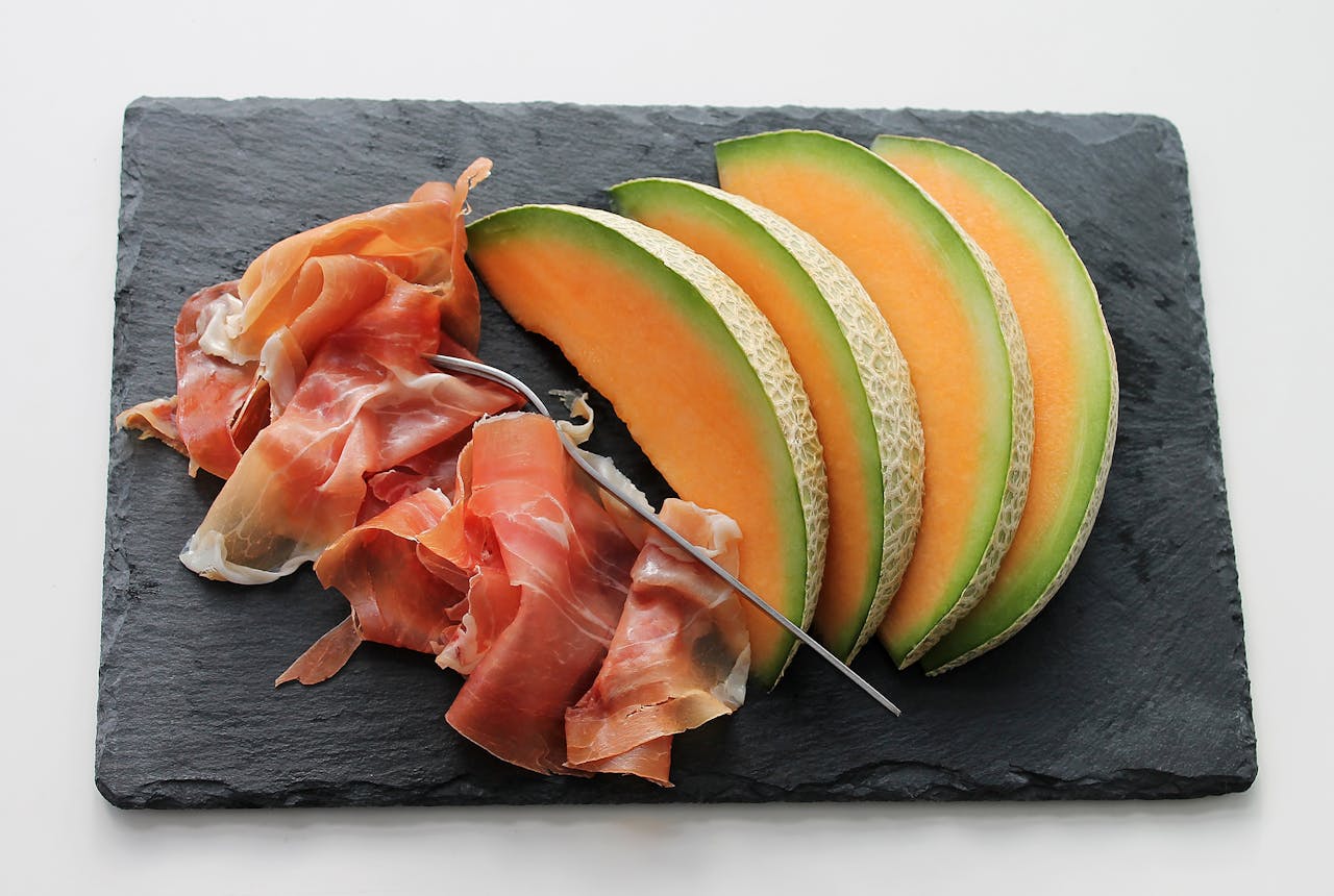 Freshly sliced melon with ham on a slate board, ideal for gourmet food concepts.