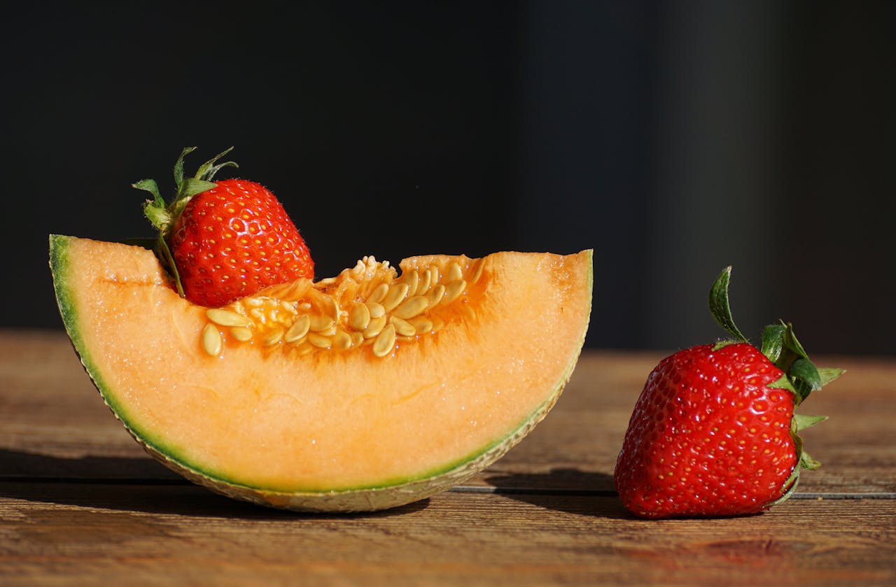 Close-up of a fresh cantaloupe slice with juicy strawberries on a wooden table.